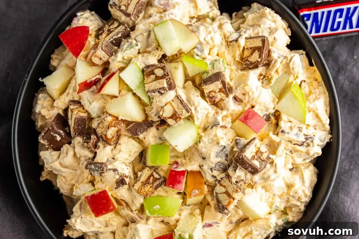 Snickers Apple Dessert Salad Recipe | Chocolate Caramel Apple Fluff 2 A bowl of creamy apple Snickers salad topped with chopped Snickers bars and red and green apple pieces.