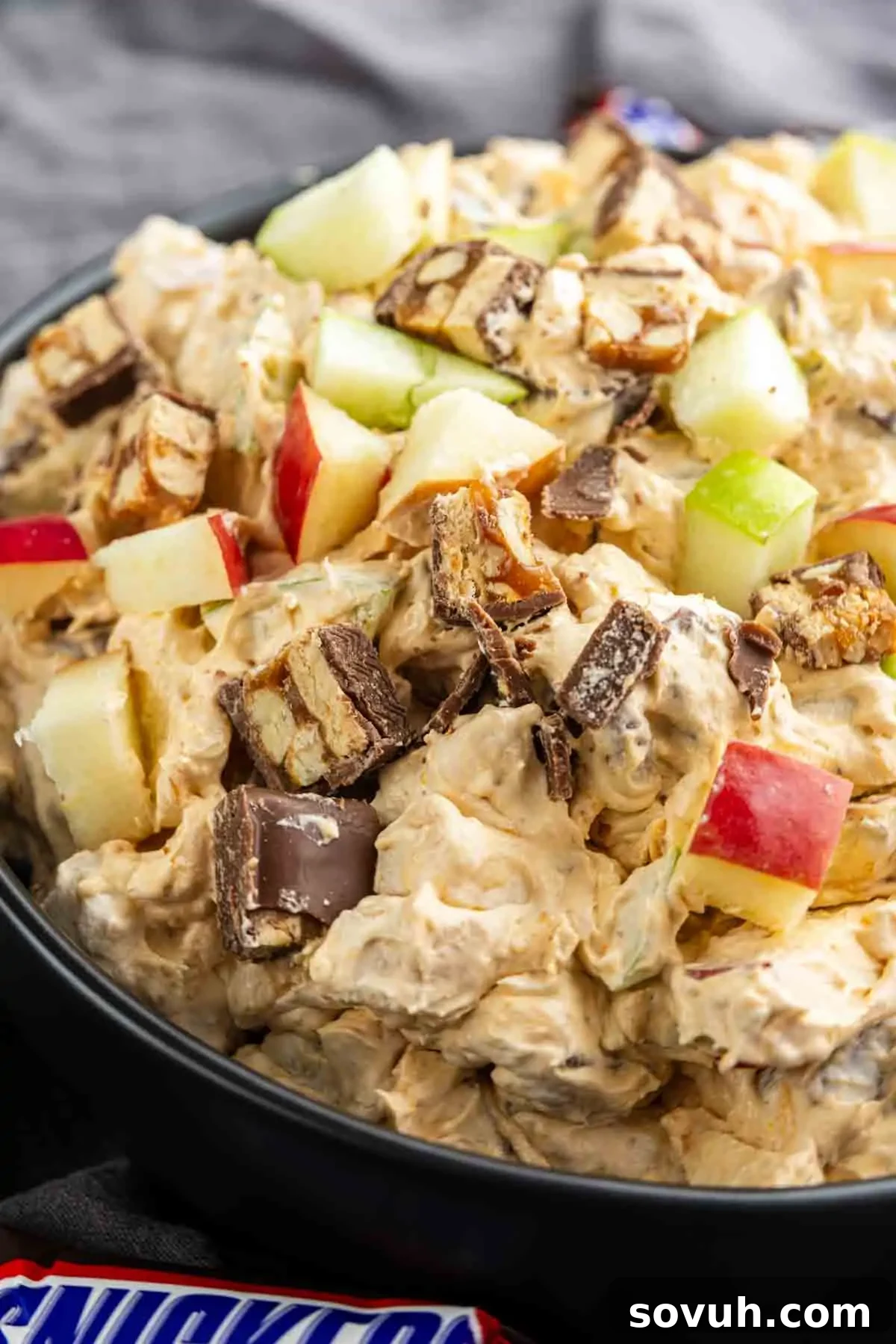 Snickers Apple Dessert Salad Recipe | Chocolate Caramel Apple Fluff 6 A bowl of creamy Snickers Salad mixed with chopped apples and pieces of chocolate candy bars.