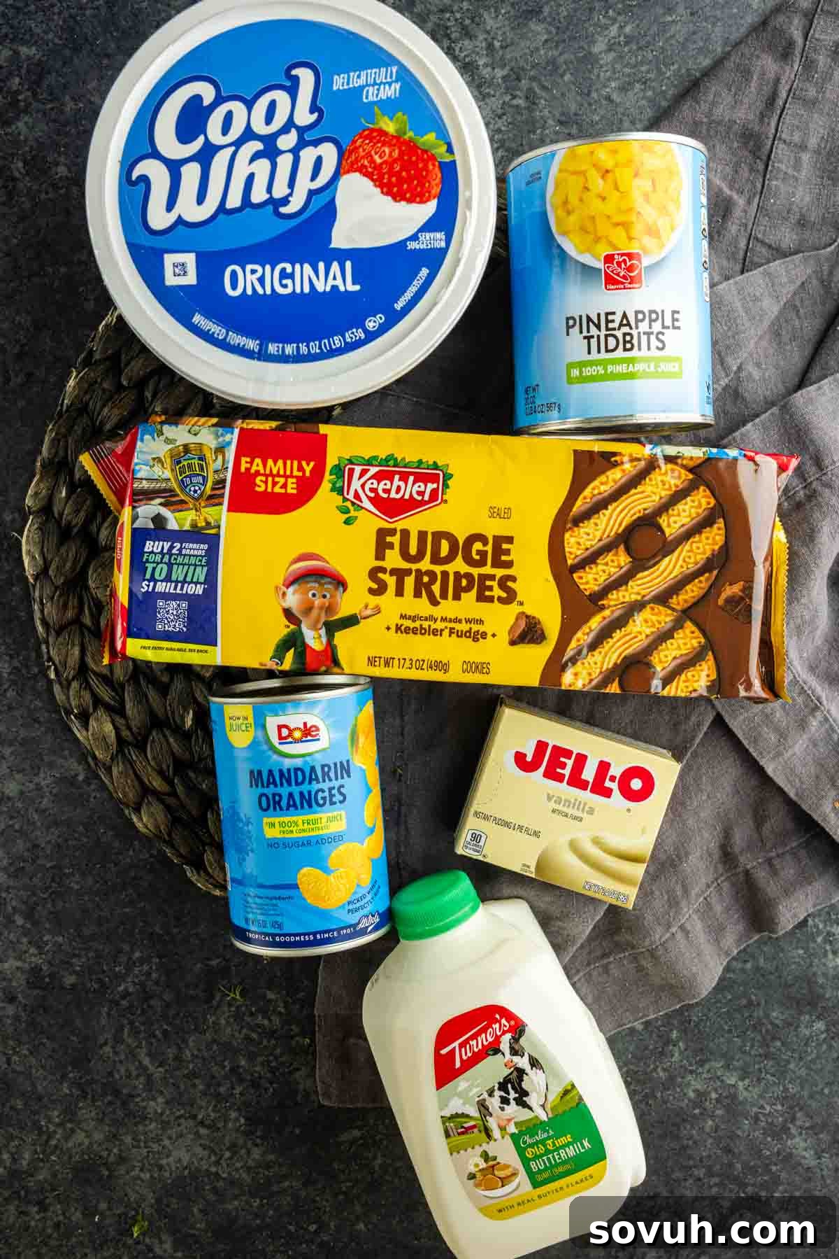 Fudge Stripe Cookie Salad Recipe: Creamy No-Bake Dessert 3 Assorted dessert ingredients for an easy Cookie Salad: Cool Whip, pineapple tidbits, Fudge Stripes cookies, mandarin oranges, vanilla Jello pudding mix, and a carton of milk arranged on a dark surface.
