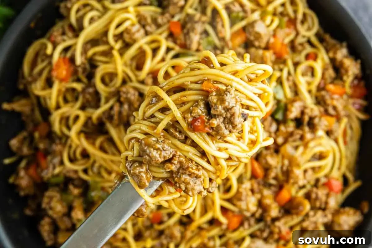 Viral Cajun Dirty Spaghetti Recipe for Dinner That Delights 2 A close-up of Cajun spaghetti with ground beef and sausage, mixed with diced red peppers and twirled on a fork above a pan filled with the flavorful pasta dish.