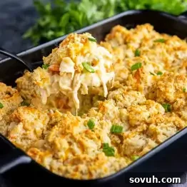 A casserole dish filled with a golden, Cheddar Bay Biscuit Chicken Casserole, with a serving being lifted out to reveal melted cheese, herbs, and tender chicken—reminiscent of a savory chicken cobbler.