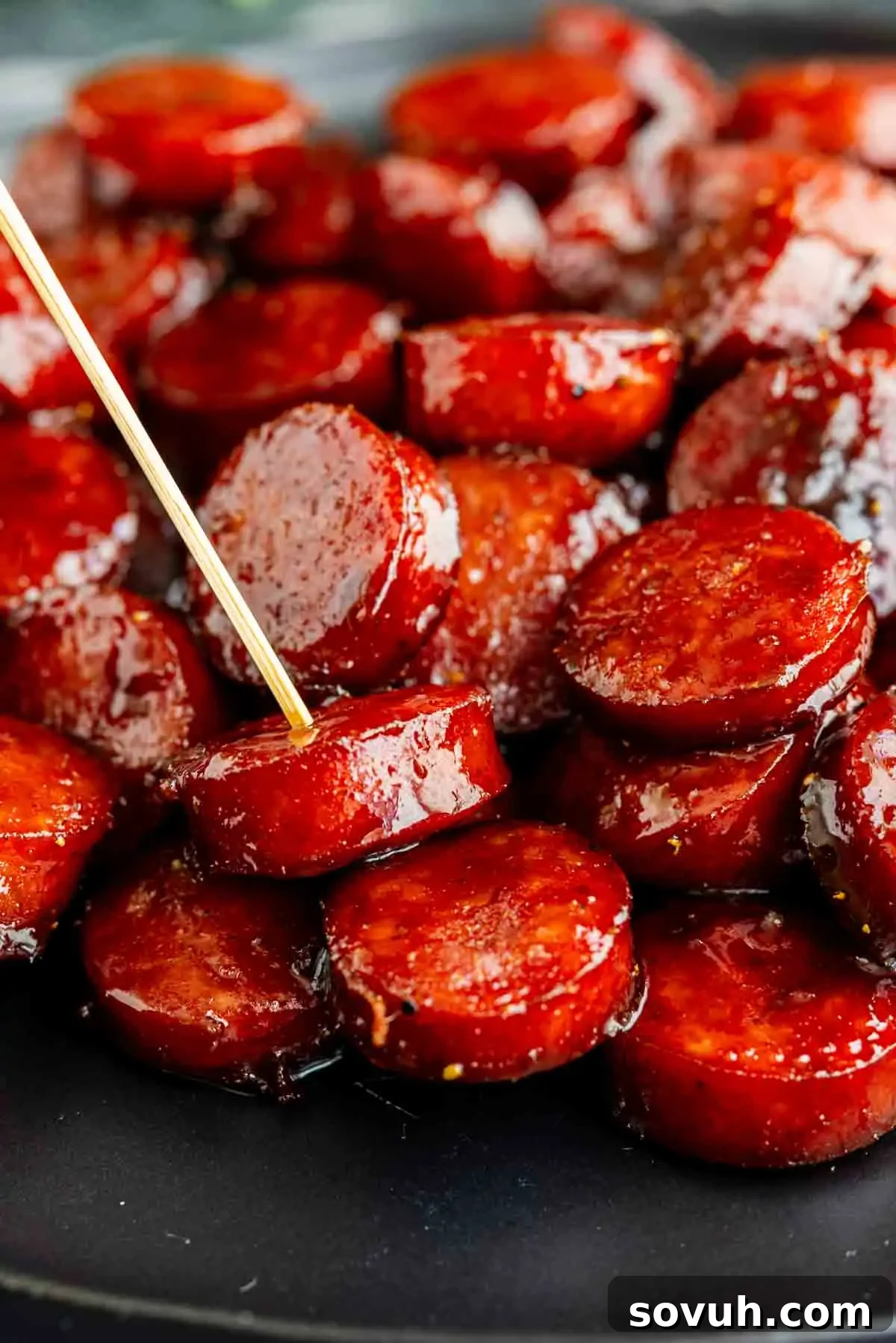 Oven-Baked Brown Sugar Barbecue Kielbasa Recipe 6 Close-up of Barbecue Brown Sugar Kielbasa bites on a black plate, with a toothpick inserted into one of the glazed sausage slices—an irresistible kielbasa appetizer recipe.