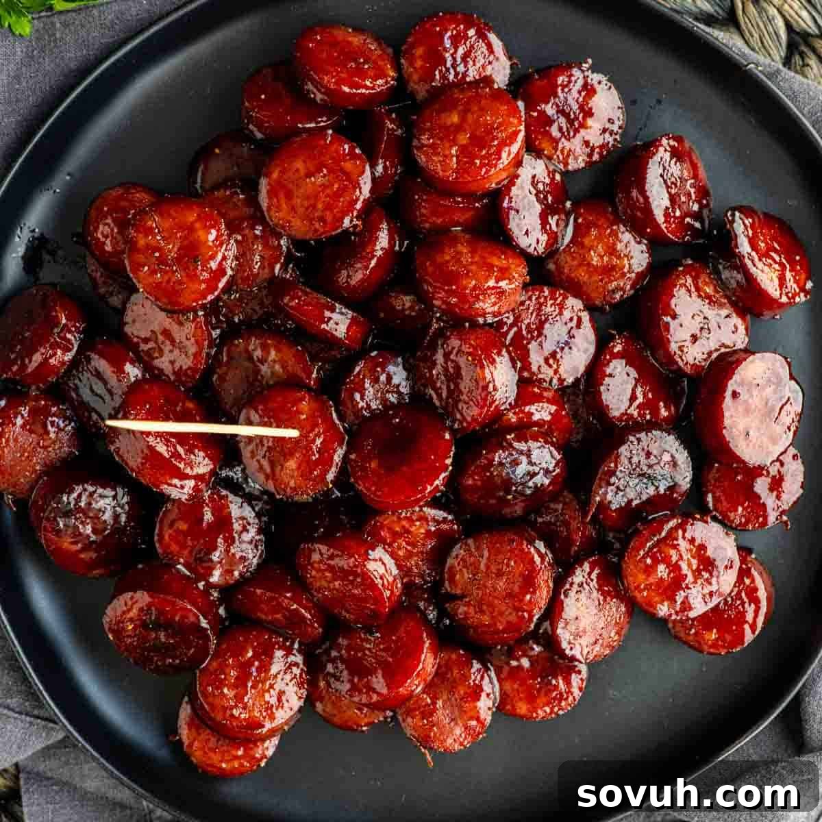 Oven-Baked Brown Sugar Barbecue Kielbasa Recipe 7 A black plate filled with glazed BBQ kielbasa bites is shown, each sliced sausage round glistening and one piece topped with a toothpick.