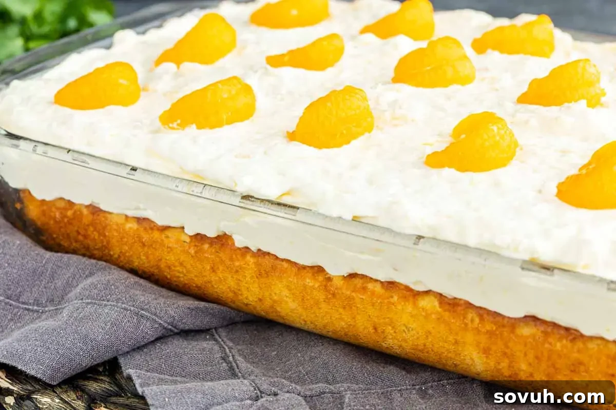 Southern Pig Pickin’ Cake with Mandarin Orange Glaze Recipe 2 A rectangular glass dish filled with a layered Southern dessert, topped with whipped cream and mandarin orange segments, sits on a light-colored cloth—reminiscent of a classic mandarin orange cake.