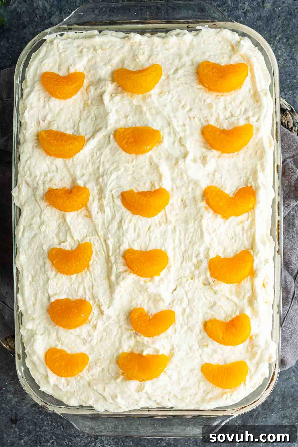 Southern Pig Pickin’ Cake with Mandarin Orange Glaze Recipe 5 Rectangular glass dish filled with a creamy mandarin orange cake, topped with evenly spaced mandarin segments in rows for a classic Pig Pickin’ Cake presentation.