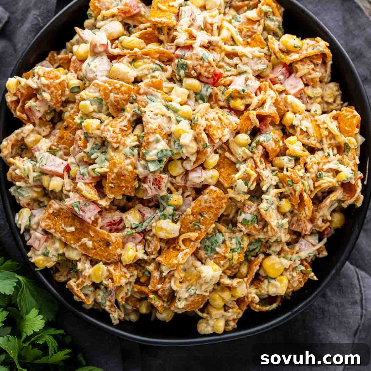 Frito Salad Recipe: Chili Cheese Corn Salad 2 A bowl filled with a creamy corn chip salad made of corn, chopped vegetables, herbs, and crushed tortilla chips mixed together.