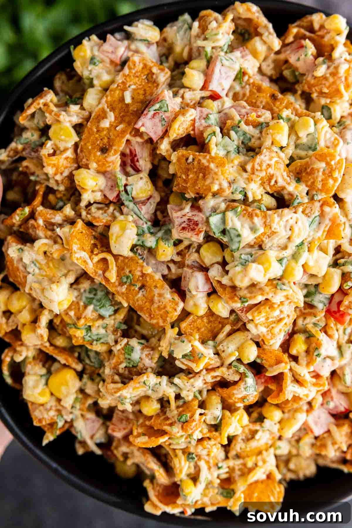 Frito Salad Recipe: Chili Cheese Corn Salad 6 A close-up of a bowl filled with creamy Frito Corn Salad, mixed with chopped vegetables, shredded cheese, and crunchy Fritos chips.