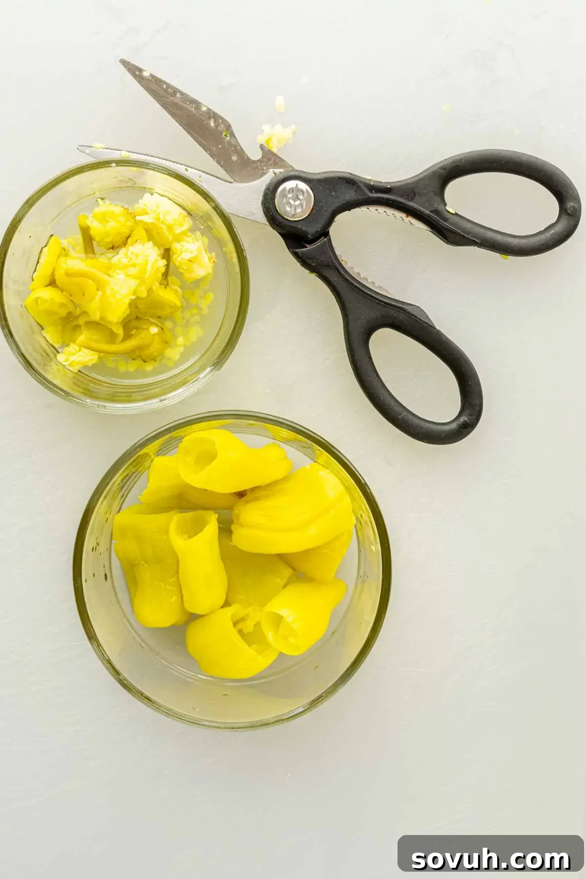 Air Fryer Stuffed Pepperoncinis with Pepperoni and Hot Honey 4 Two glass bowls with chopped yellow pickled peppers, ideal for making pepperoncini poppers or air fryer stuffed pepperoncinis, sit beside a pair of black kitchen scissors on a white surface.