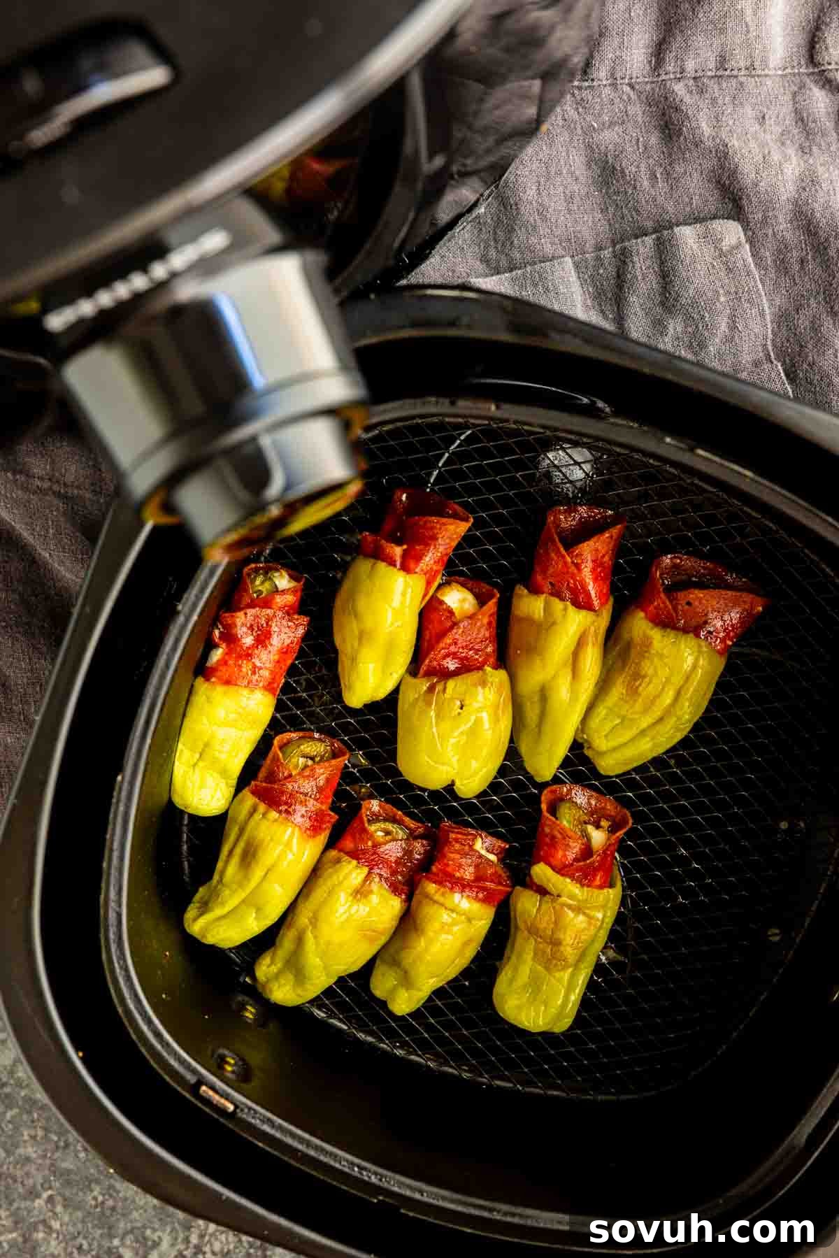 Air Fryer Stuffed Pepperoncinis with Pepperoni and Hot Honey 7 Yellow peppers wrapped in red meat slices are arranged in an air fryer basket, ready to become delicious air fryer stuffed pepperoncinis for a quick and tasty treat.