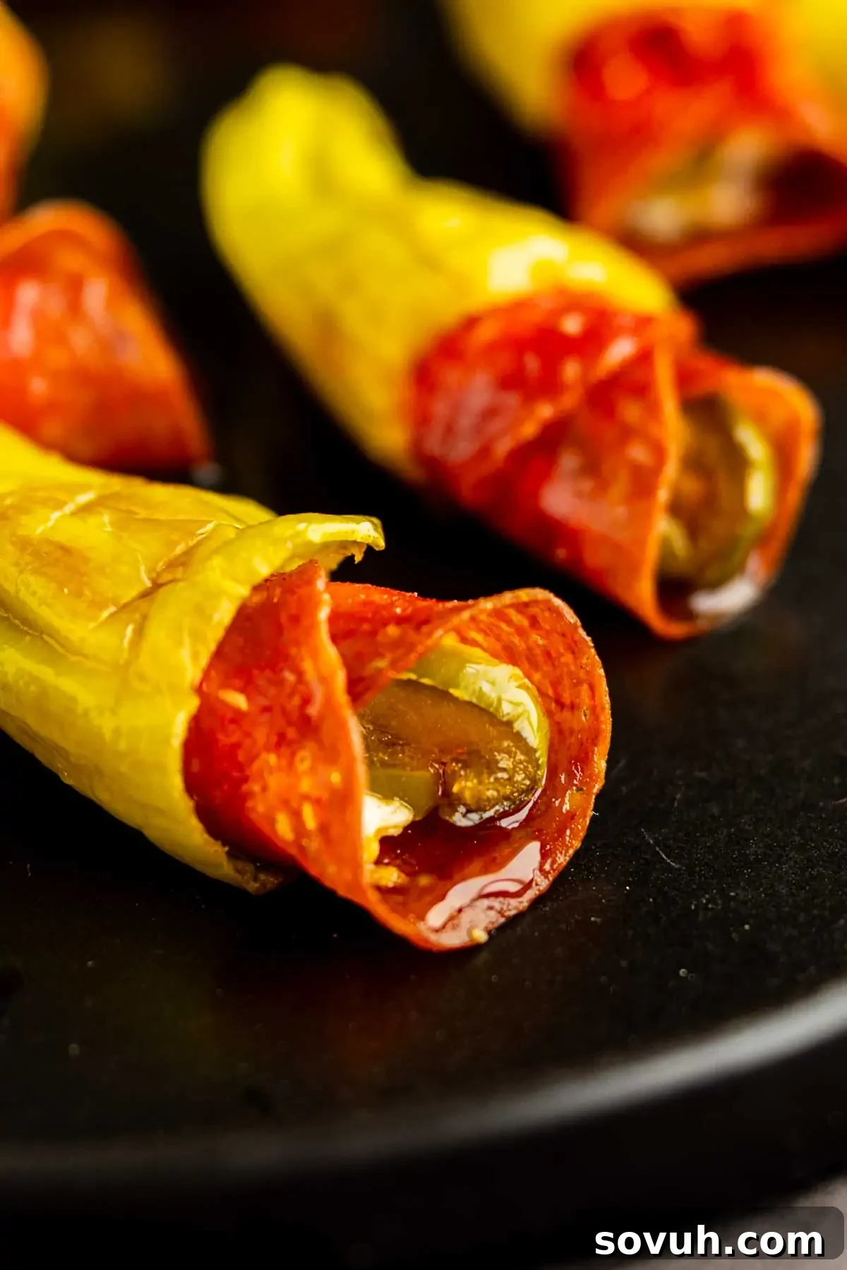 Air Fryer Stuffed Pepperoncinis with Pepperoni and Hot Honey 8 Close-up of yellow pepper slices stuffed with pepperoni and melted cheese on a black plate, reminiscent of flavorful stuffed pepperoncinis.