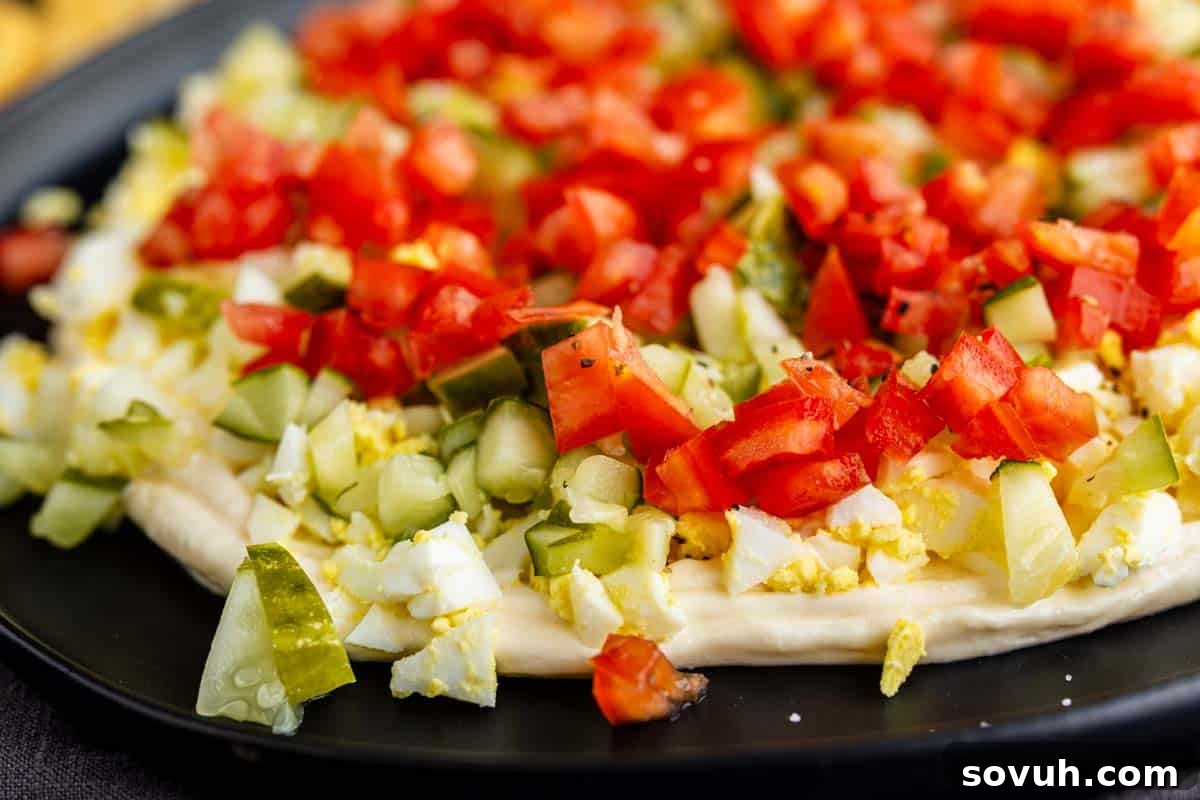Viral TikTok Layered Egg Salad Dip Recipe 2 Close-up of a flatbread topped with chopped hard-boiled eggs, diced pickles, and diced tomatoes on a black plate—an easy twist on the popular TikTok egg salad dip.