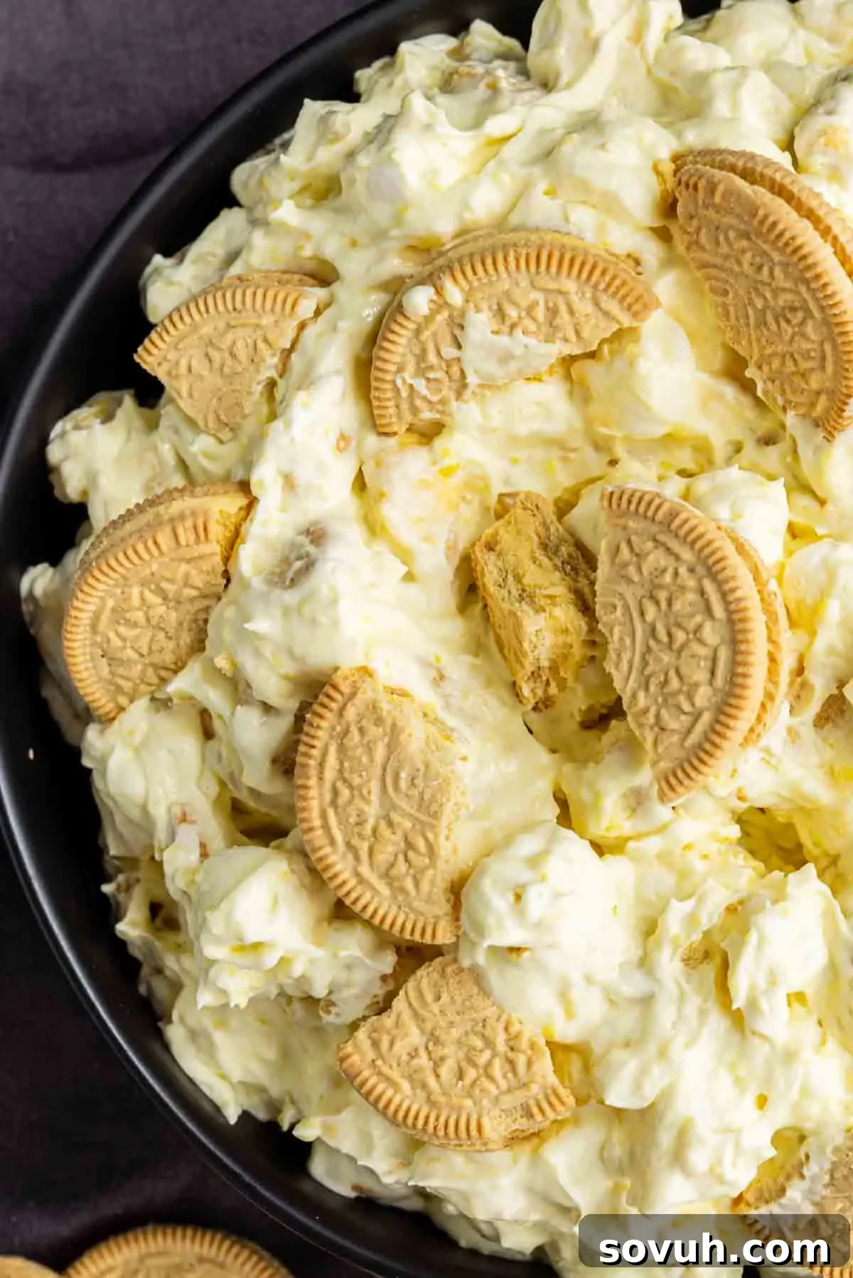 Lemon Cookie Salad: Bright Midwestern Dessert Twist 5 A close-up of a lemon dessert salad with a creamy, yellowish mixture and pieces of golden sandwich cookies on top, served in a black bowl—an irresistible take on the classic lemon fluff.