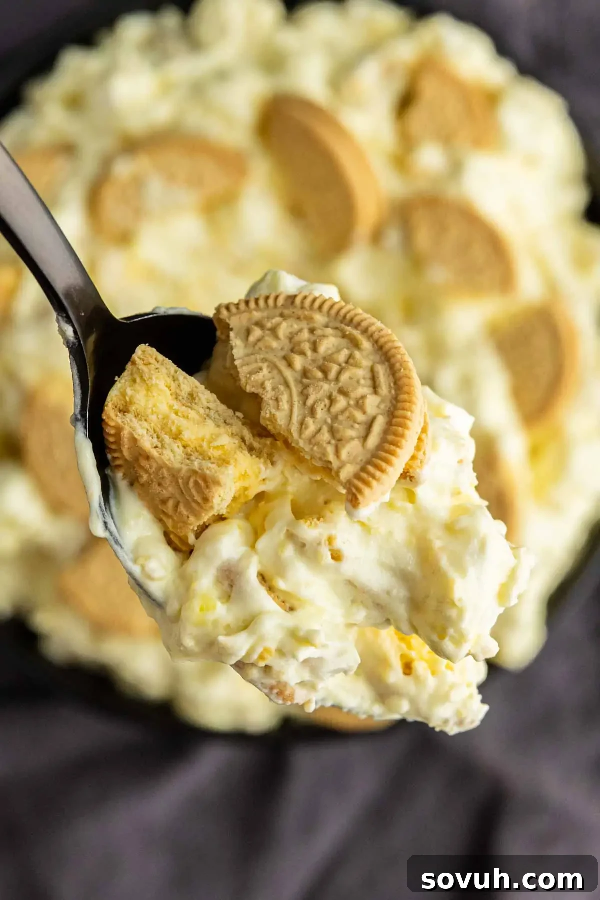 Lemon Cookie Salad: Bright Midwestern Dessert Twist 6 A close-up of a spoonful of creamy lemon fluff dessert with crushed golden sandwich cookies, held above a dish of the same lemon dessert.