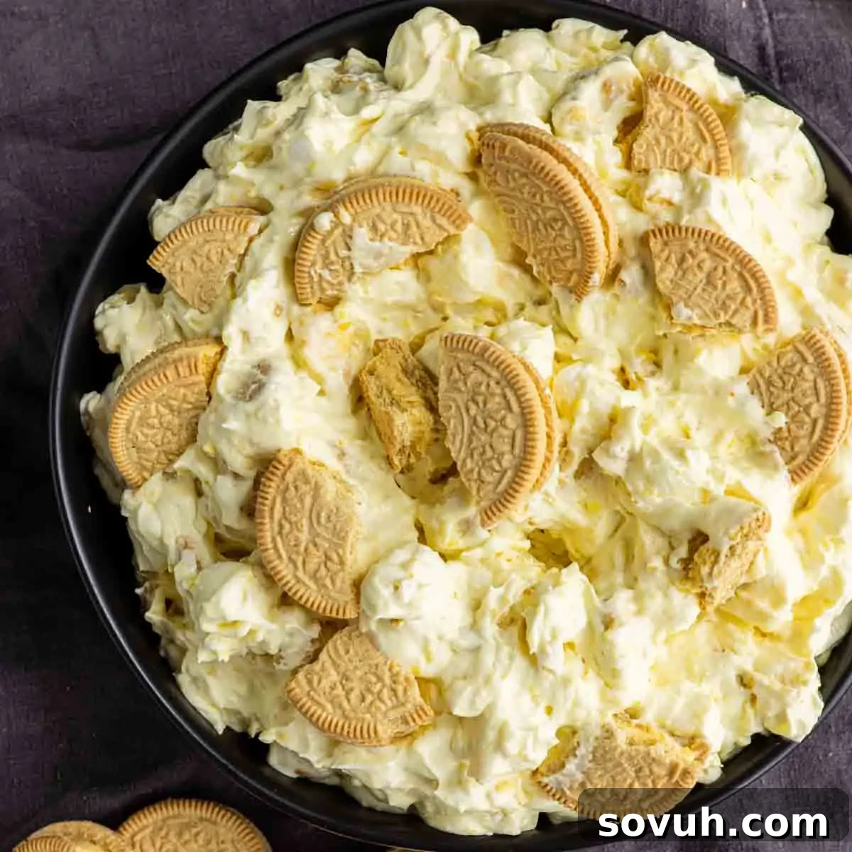 Lemon Cookie Salad: Bright Midwestern Dessert Twist 7 A bowl filled with a creamy lemon dessert salad topped with pieces of golden sandwich cookies, displayed on a dark surface.