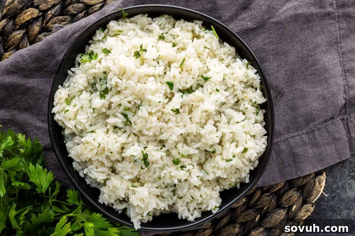 Fluffy Coconut Lime Rice Recipe with Fresh Citrus Flavor 2 A bowl of easy coconut lime rice garnished with chopped parsley, placed on a dark cloth and woven mat.