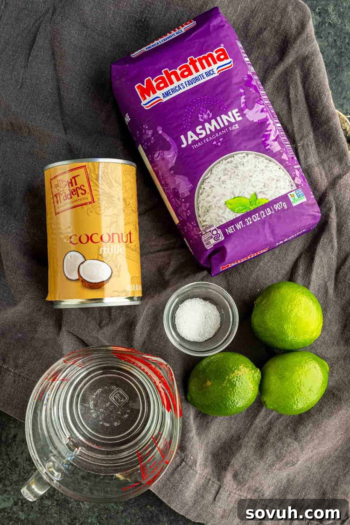 Fluffy Coconut Lime Rice Recipe with Fresh Citrus Flavor 3 A can of coconut milk, jasmine rice, three limes, a bowl of salt, and a measuring cup of water sit on a dark countertop—perfect for making easy coconut lime rice.