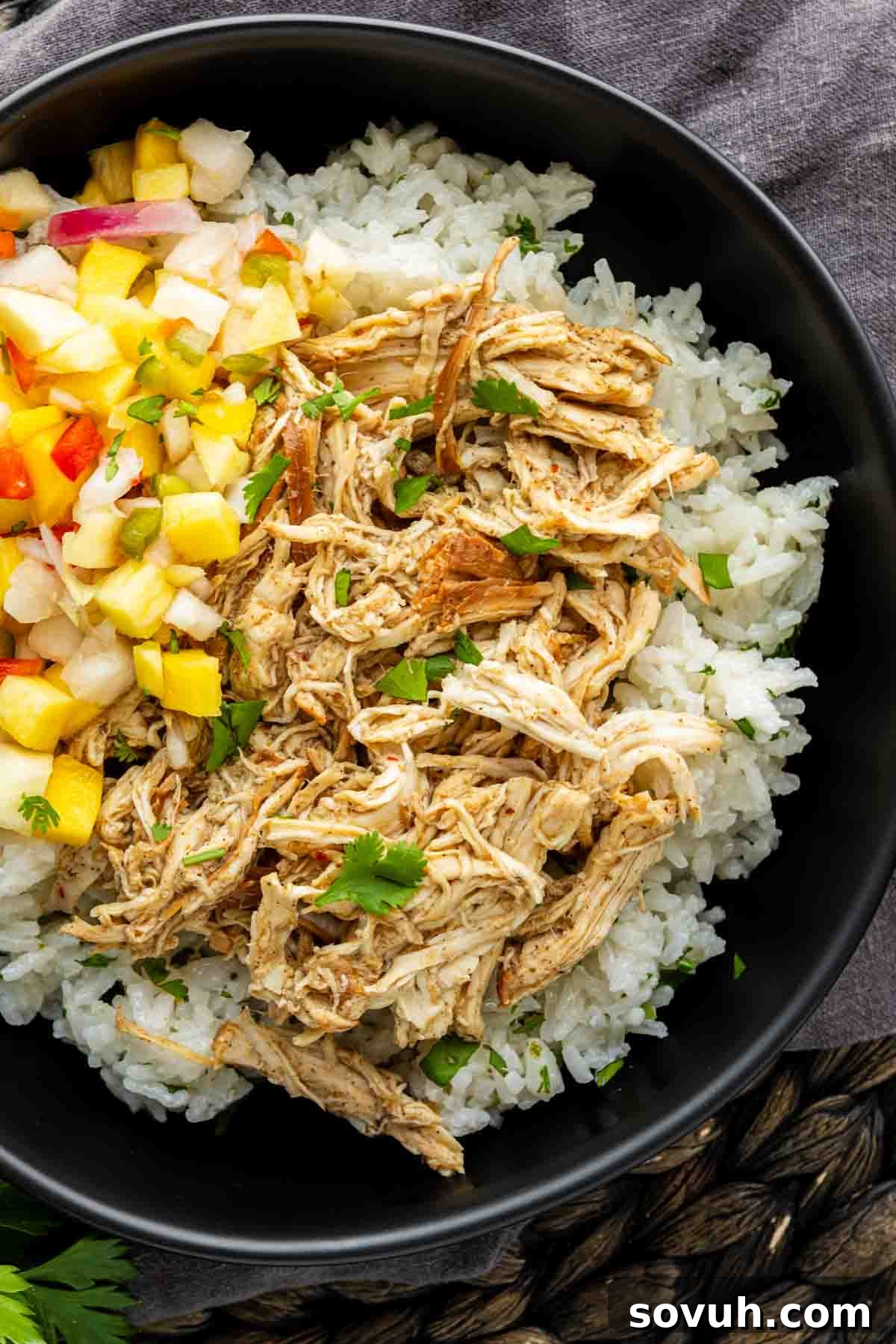 Slow Cooker Jerk Chicken Recipe 6 A black bowl filled with white rice, shredded chicken, and a colorful diced fruit salsa, garnished with fresh herbs.