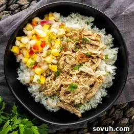Slow Cooker Jerk Chicken Recipe 8 A black bowl with white rice, tender slow cooker jerk chicken, and a colorful fruit salsa on top, placed on a dark fabric surface.