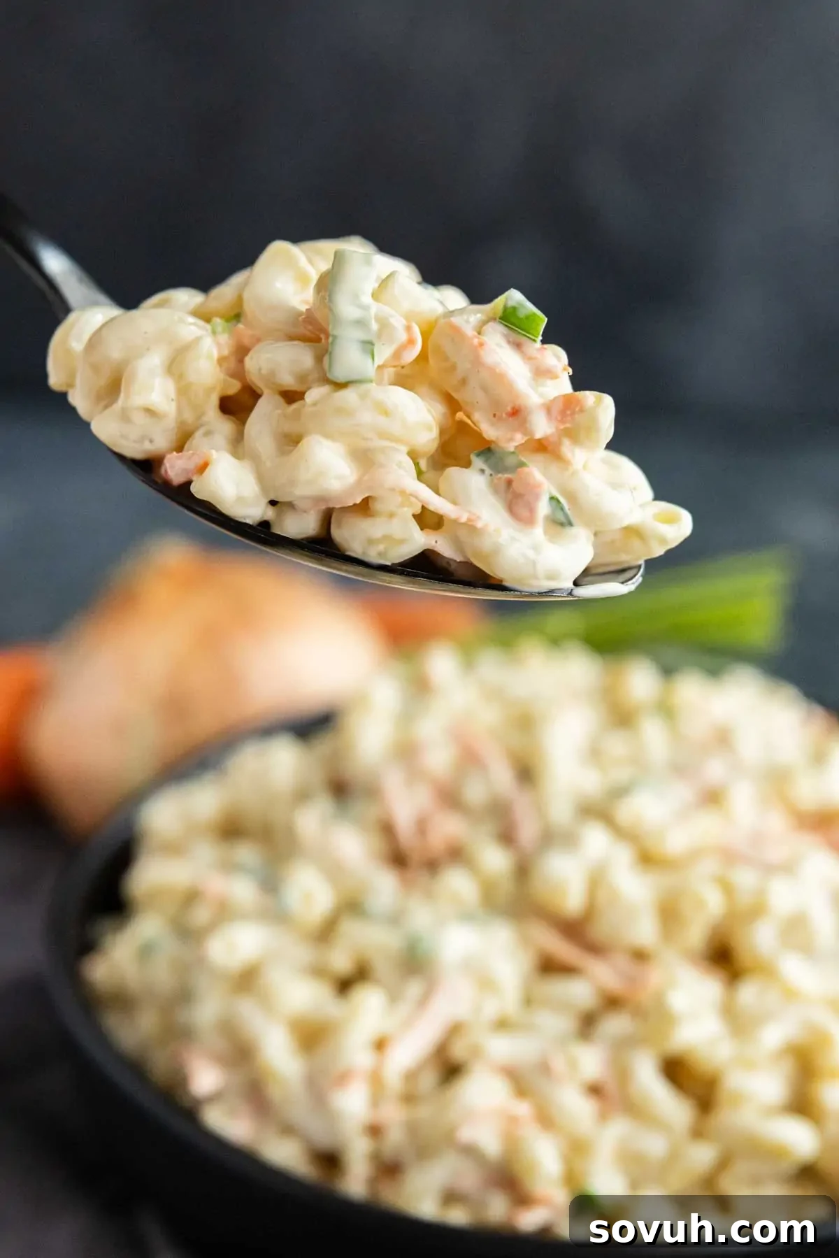 A spoonful of creamy Hawaiian macaroni salad with vegetables is held above a bowl filled with more macaroni salad—an easy potluck side dish that's perfect for any Hawaiian plate lunch.