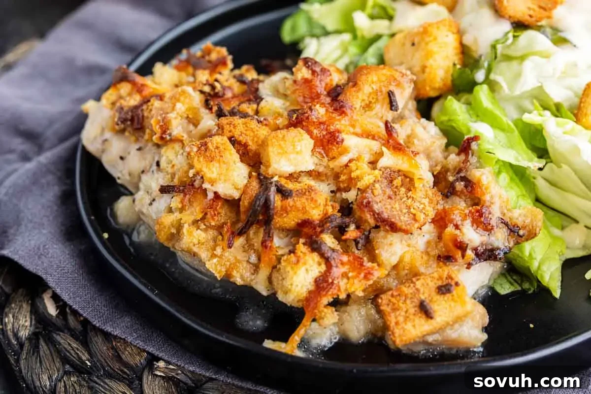 A plate with a baked Caesar chicken dish, topped with golden-brown stuffing, sits next to a green lettuce salad with croutons.