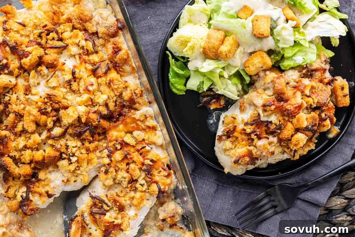 Baked chicken breasts topped with stuffing and cheese in a casserole dish make this easy chicken casserole a comfort food favorite, served on a plate with Caesar salad, croutons, and a touch of Caesar dressing for the perfect Chicken Caesar Bake experience.