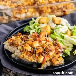 A plate of baked Caesar chicken topped with savory stuffing and melted cheese, served with a side of lettuce salad and crunchy croutons.