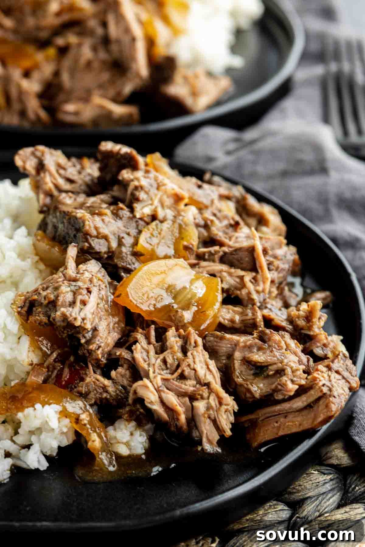 Shredded beef with cooked onions, reminiscent of a Slow Cooker Georgia Pot Roast, served over white rice on a black plate.