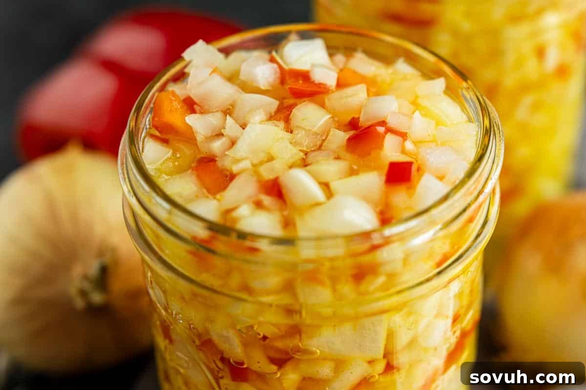 A close-up of a glass jar filled with chopped onions and red peppers in a liquid, with whole onions and a red bell pepper in the background.